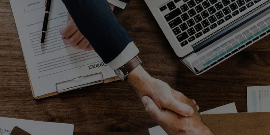 Aperto de mão entre dois homens por cima da secretária com portátil e crm